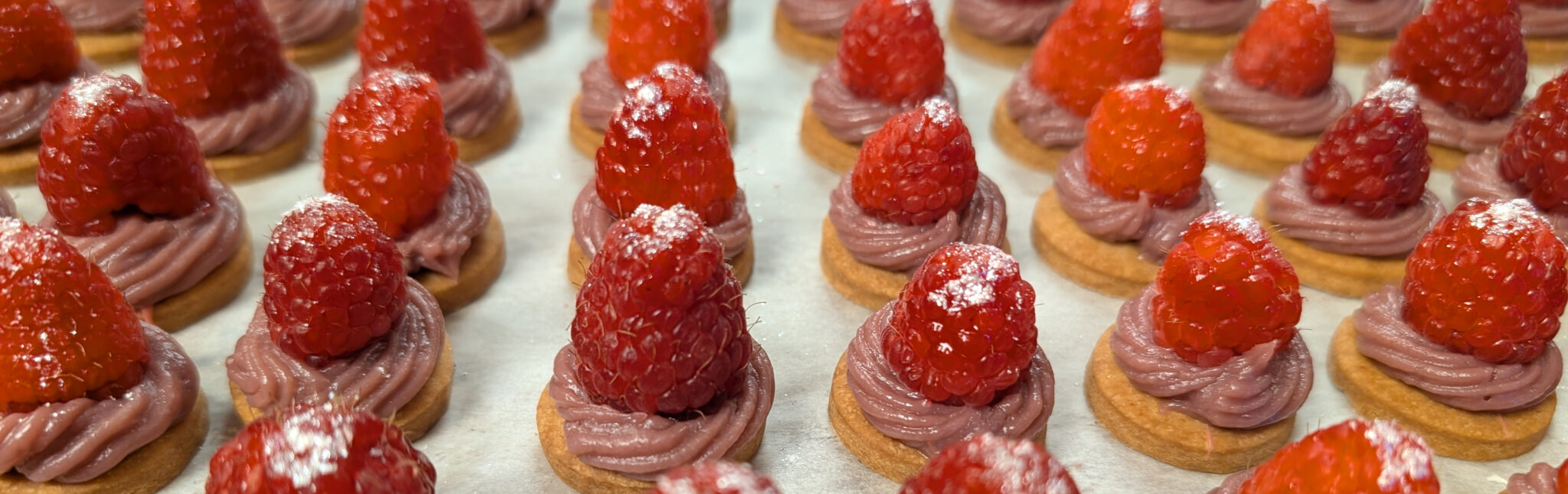 Holiday VIP desserts for a Total Wine event. Round cookies with a piped swirl of pink ganache, topped with a silver-sprinkled fresh raspberry. 