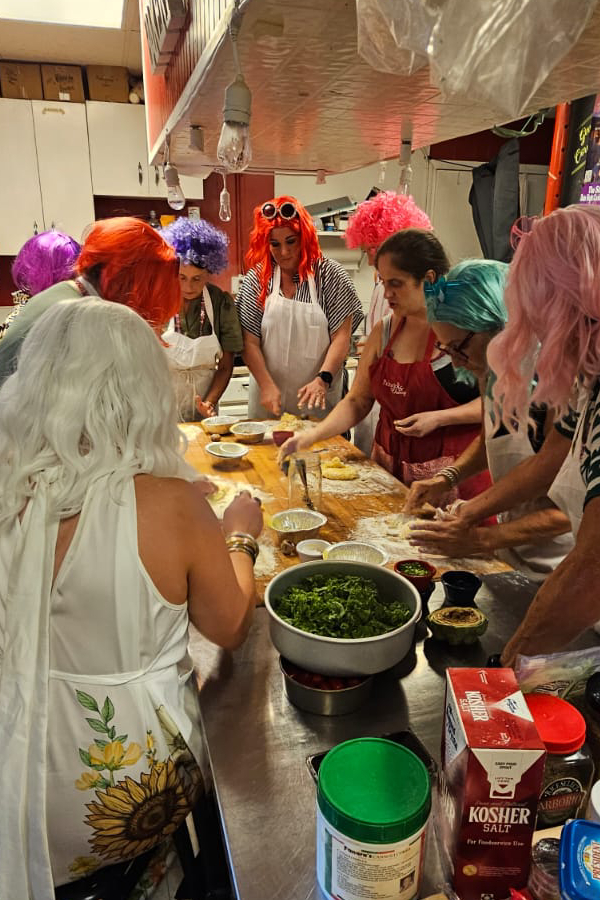Guests in brightly colored wigs cooking together during a private bachelorette party at Pickwick & Cherry