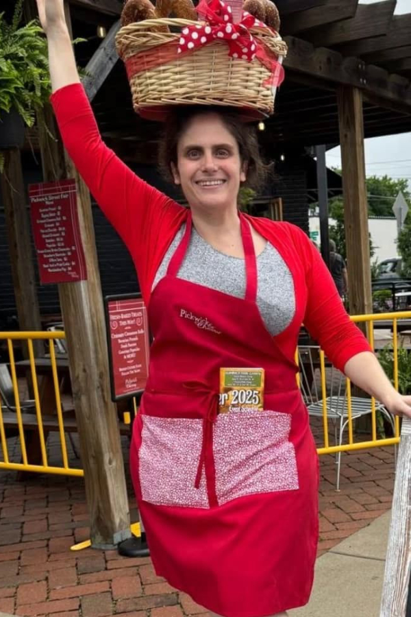 Pickwick & Cherry owner Katie Kring balancing a basket of pretzels on her head to sell them at the Pickwick Street Fair. She is wearing a red apron.